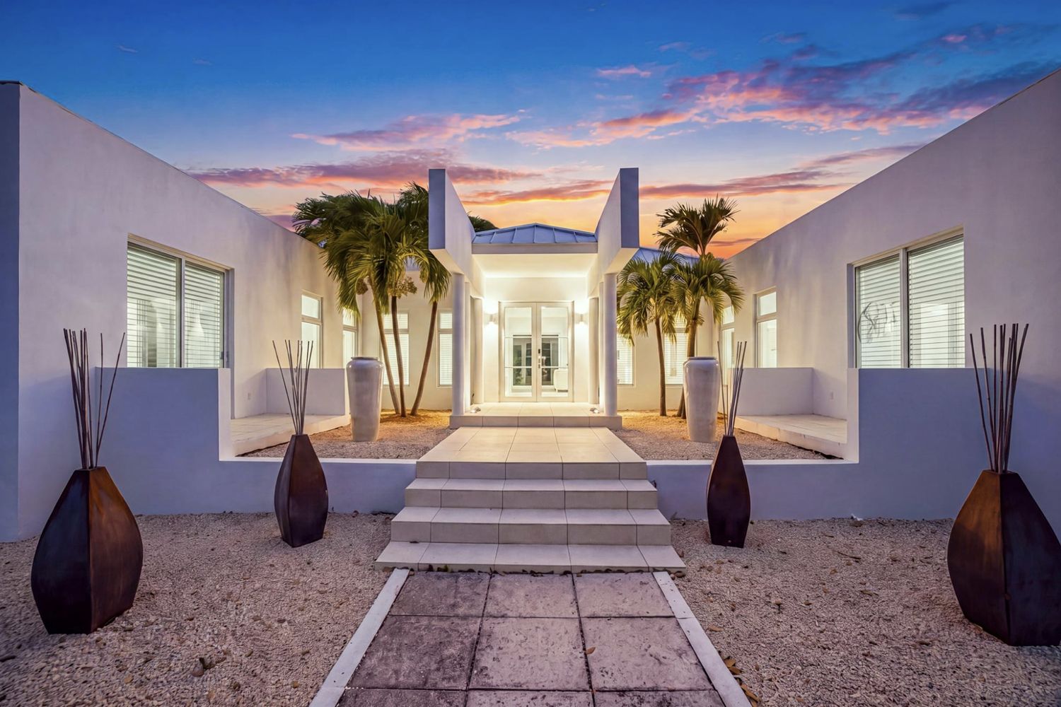 Entrance court of Villa Solemar at dusk, white walls framing palms and the double front doors
